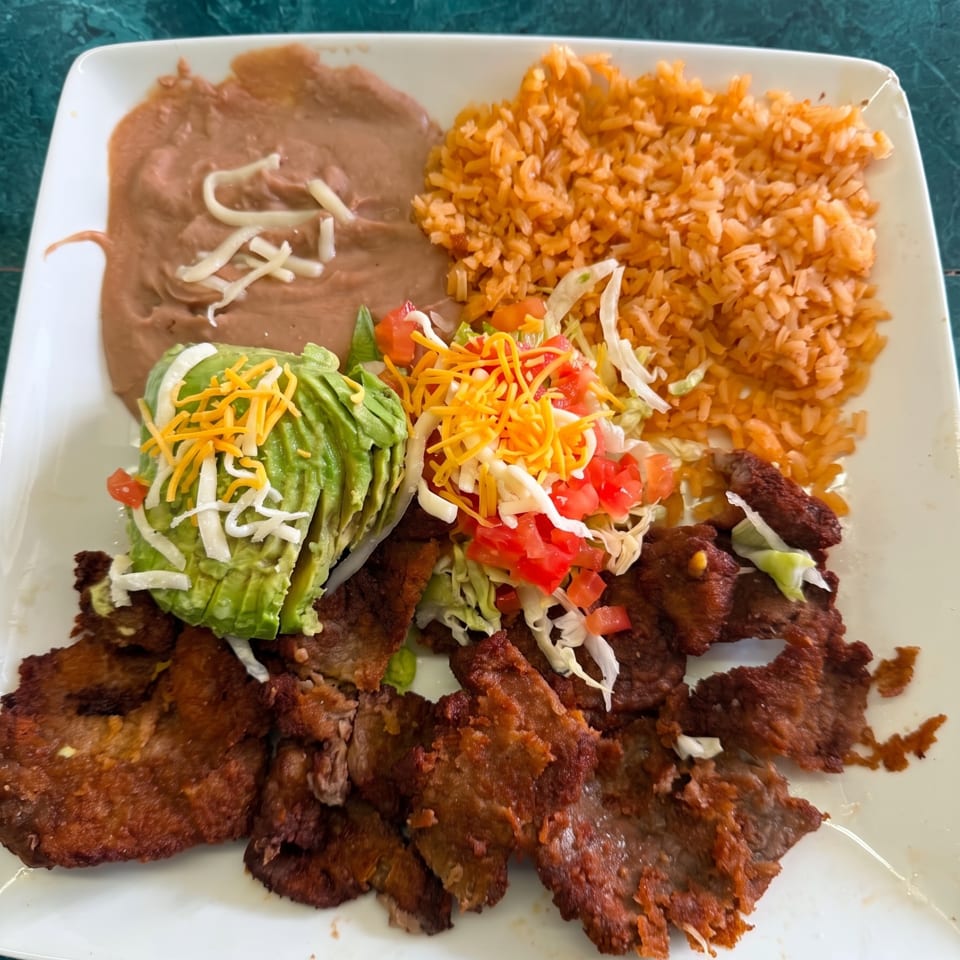 A plate of carne asada, refried beans, rice, and a salad with avocado, cheese, and tomatoes.